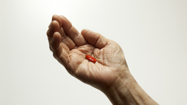 A person holding VYNDAMAX (tafamidis) capsule, capsule pictured is not actual size